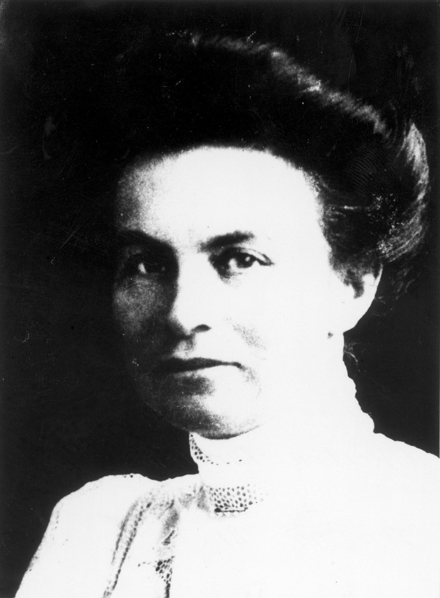Portrait en noir et blanc d’une femme aux cheveux relevés et au chemisier à col montant, qui regarde gravement l’objectif.