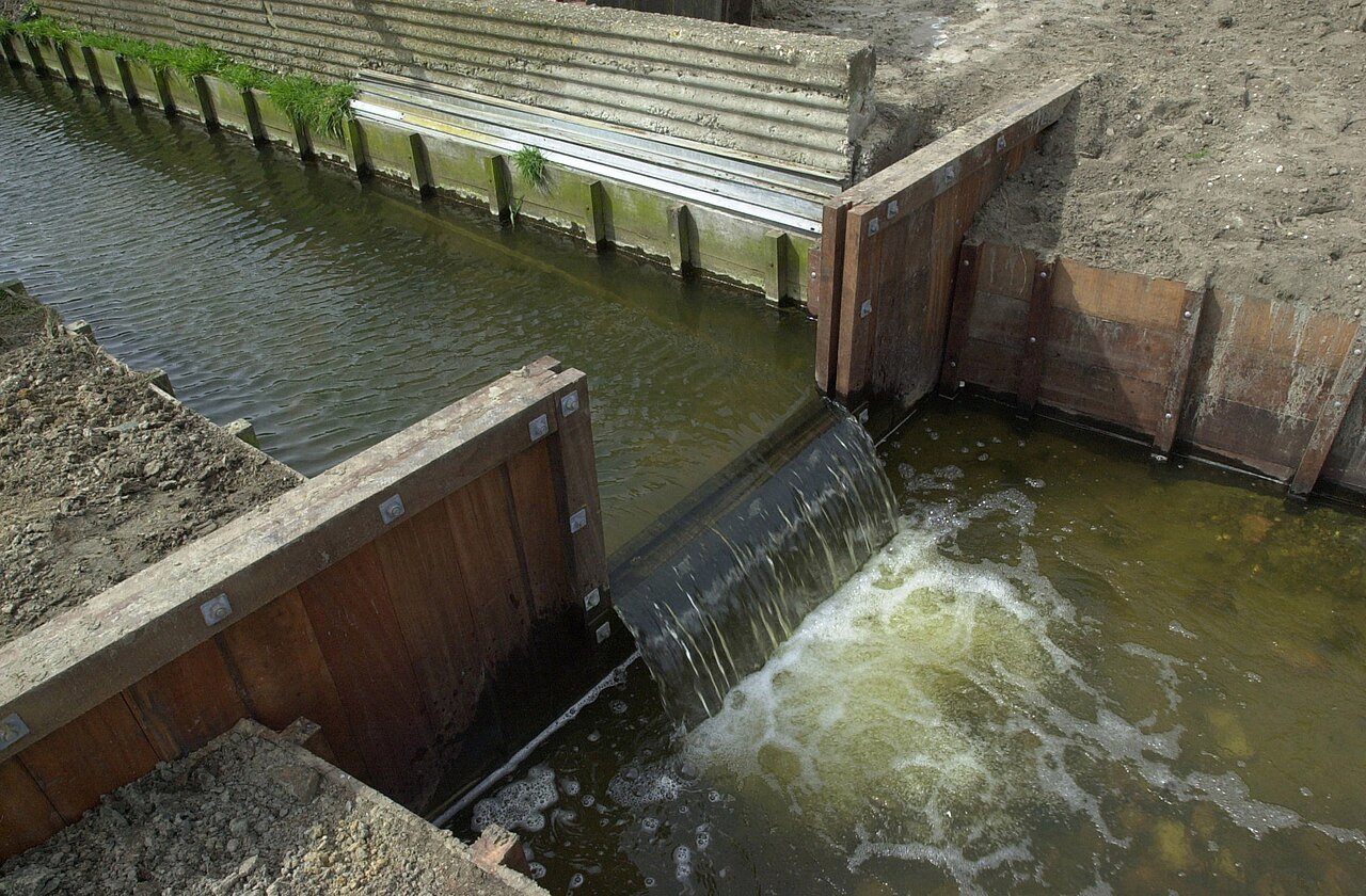 Water stroomt over een stuw in een sloot