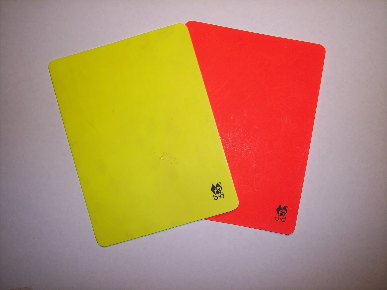 Een gele en een rode plastic kaart naast elkaar op een lichte ondergrond.