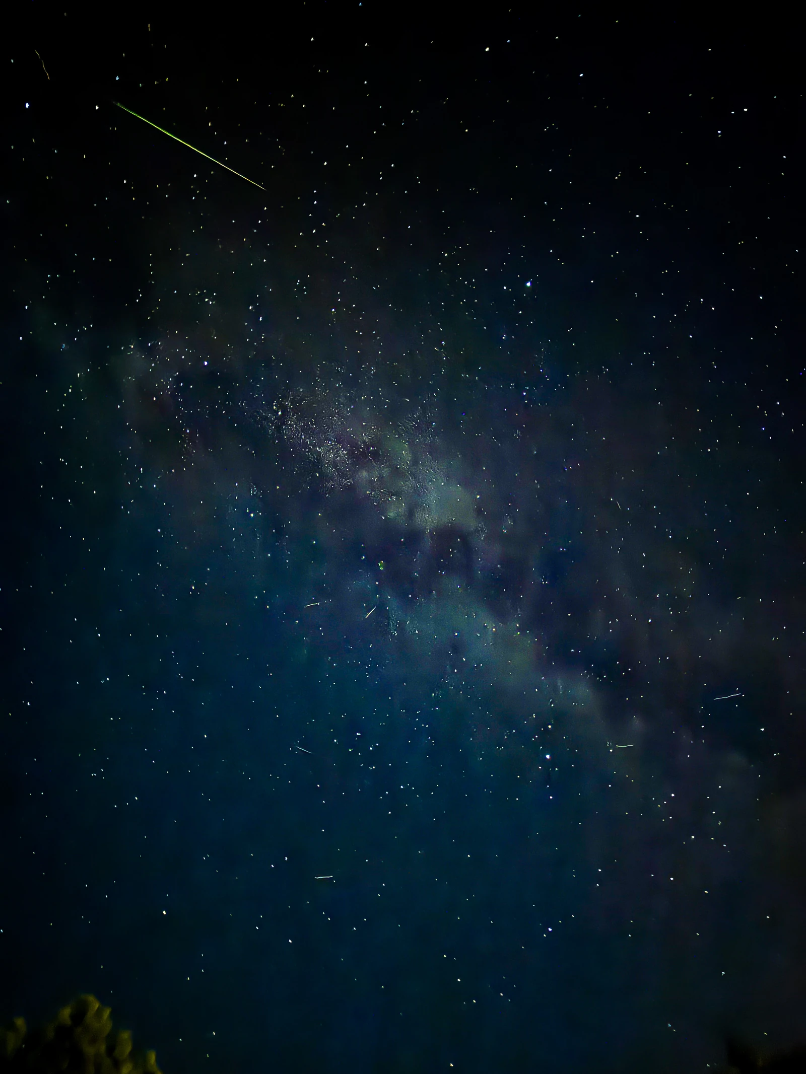 Un ciel étoilé sombre avec la Voie lactée et, en haut à gauche, la traînée verte et brillante d’un météore.