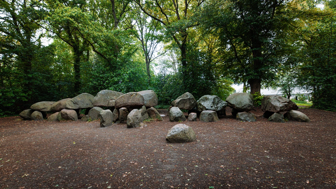 Een rij grote dekstenen op draagstenen onder bomen.