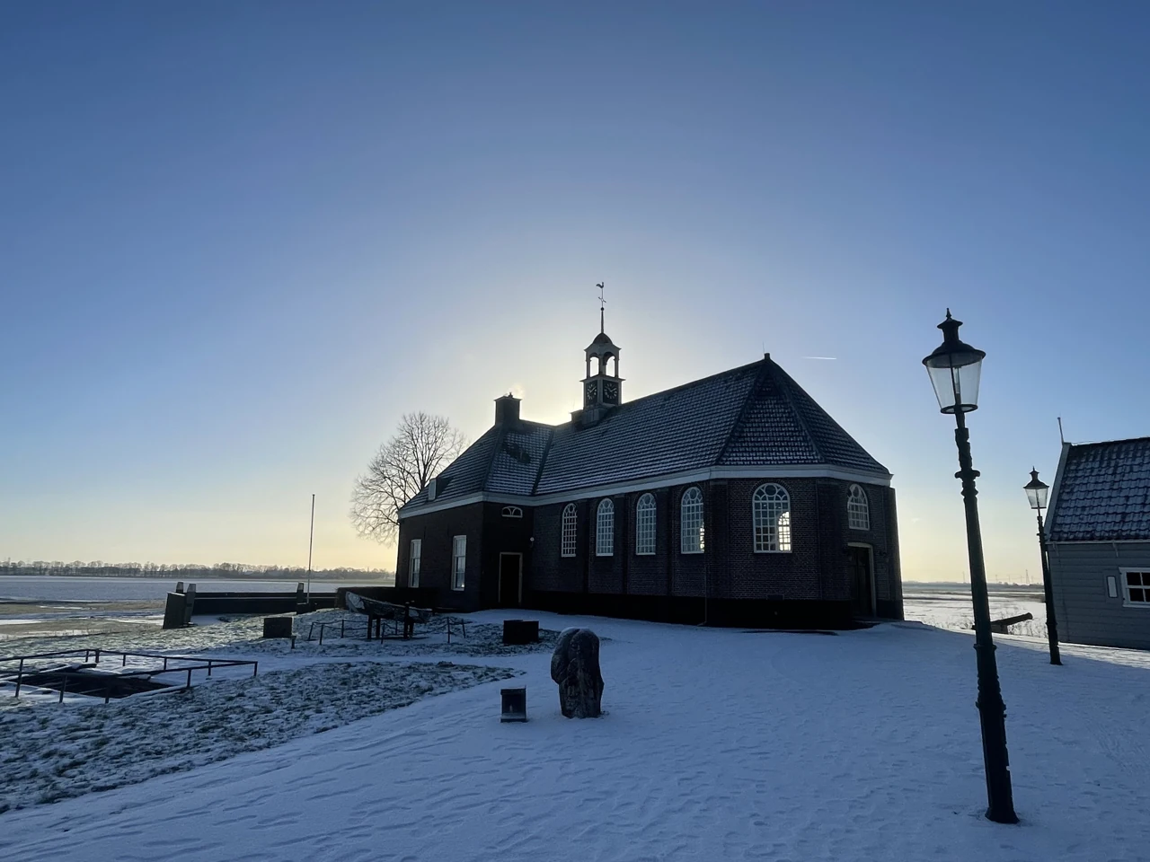 Een bakstenen kerk met klokkentoren op een besneeuwd terrein in de polder.